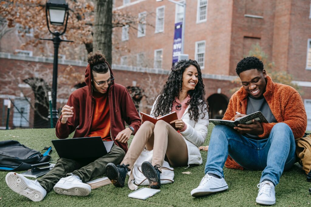 College students sitting on grass, studying, laughing